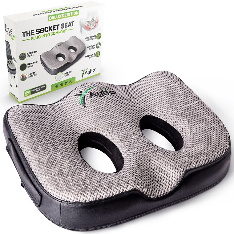 The Socket Seat at a three-quarter angle with its retail box standing behind it: gray mesh top, two oval openings side by side, a contoured rear edge and a black non-slip base.